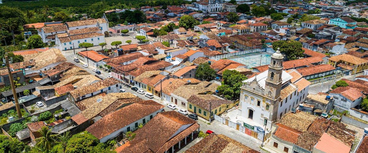 A historic town with terracotta-roofed buildings, a prominent church, and a river in the background.