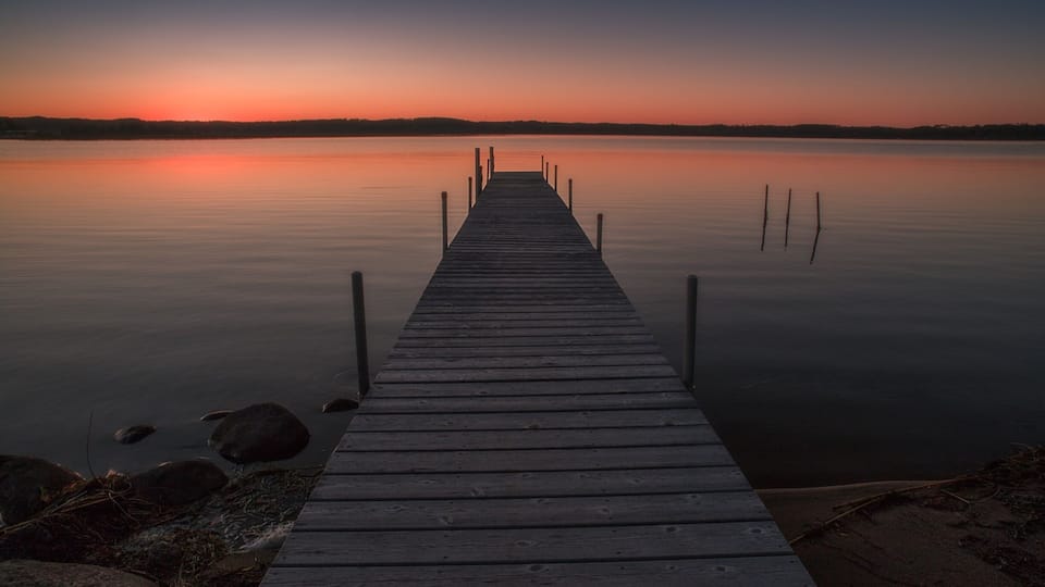 A wooden pier extending into calm water with a sunset in the background.