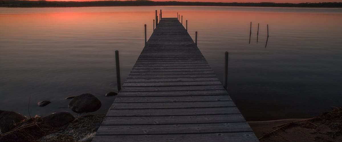 A wooden pier extending into calm water with a sunset in the background.