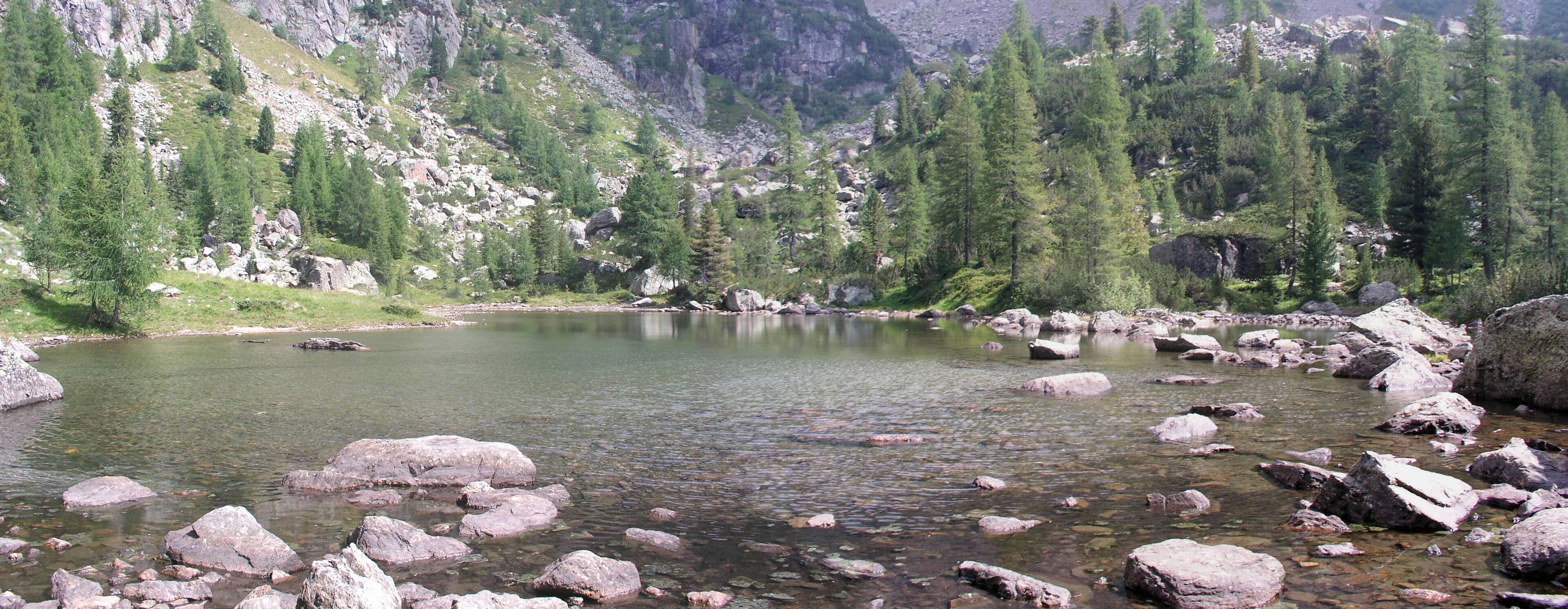A clear mountain lake surrounded by rocky terrain and dense forest.
