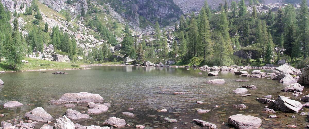 A clear mountain lake surrounded by rocky terrain and dense forest.