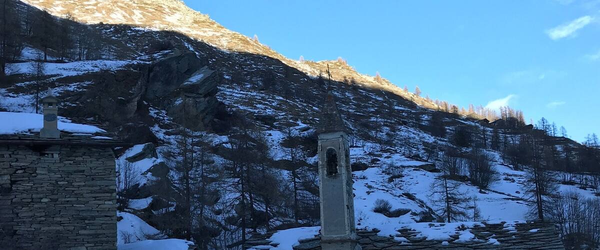 A stone church with a bell tower, surrounded by snow-covered mountains and trees.