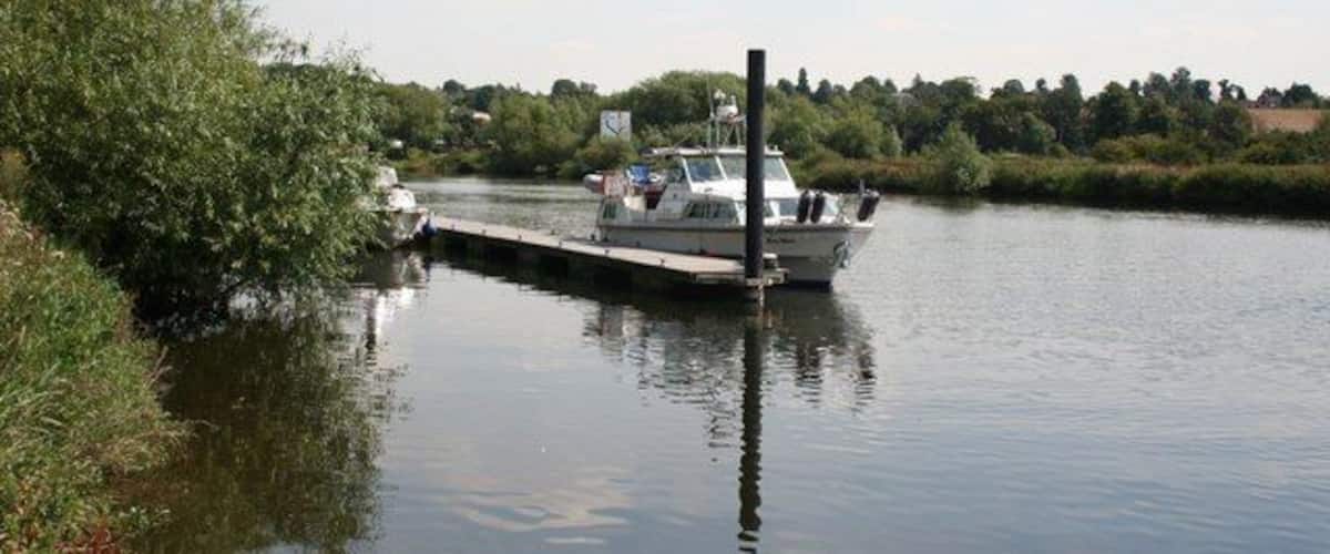 Un canal estrecho con un barco amarrado en un muelle, rodeado de follaje y árboles.