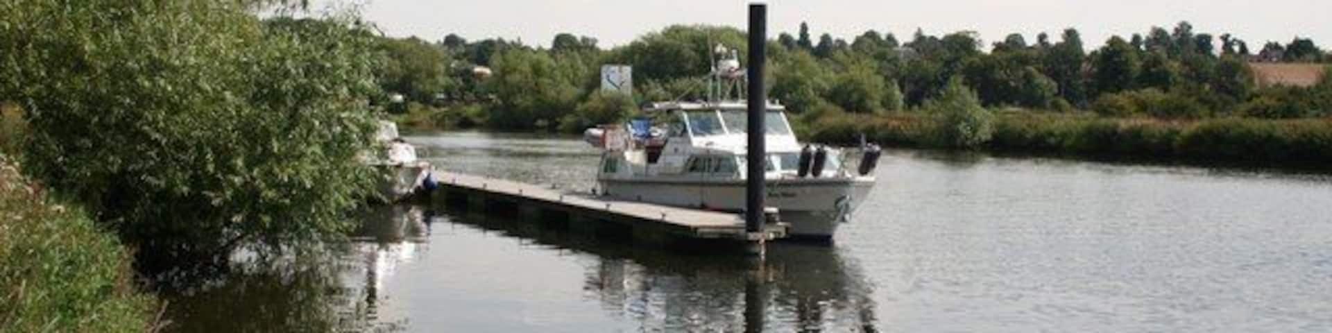 A narrow waterway with a boat docked at a pier, surrounded by greenery and trees.