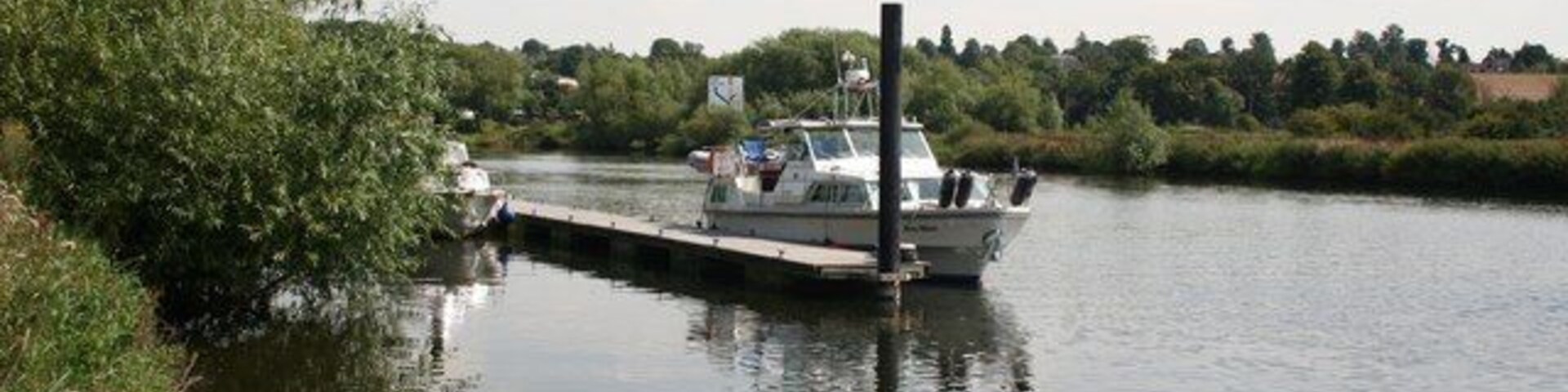 Un canal estrecho con un barco amarrado en un muelle, rodeado de follaje y árboles.