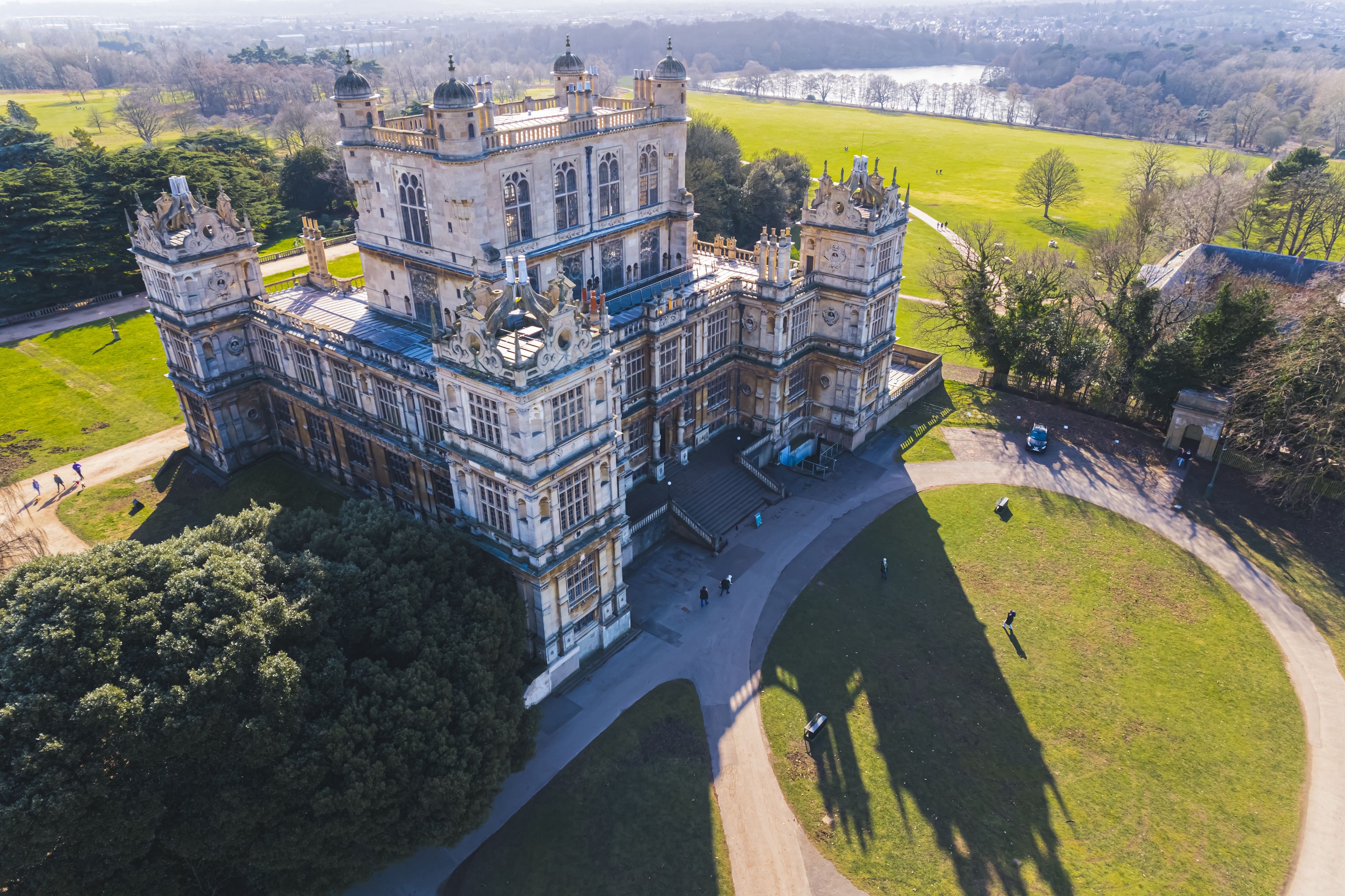 A large, ornate castle with multiple towers and turrets, surrounded by lush green lawns and trees.