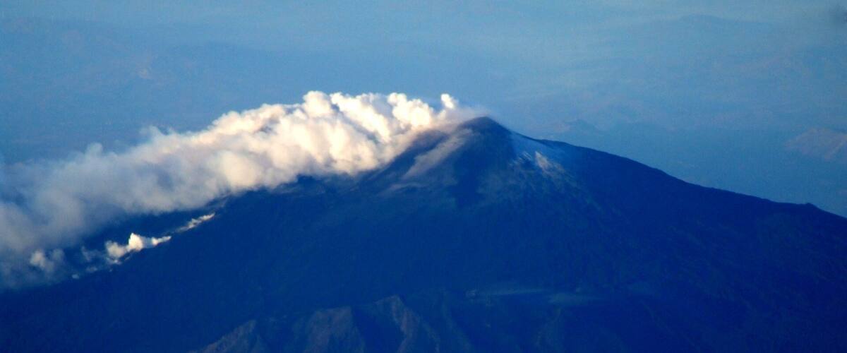 A mountain with a cloud-covered peak and a clear sky.