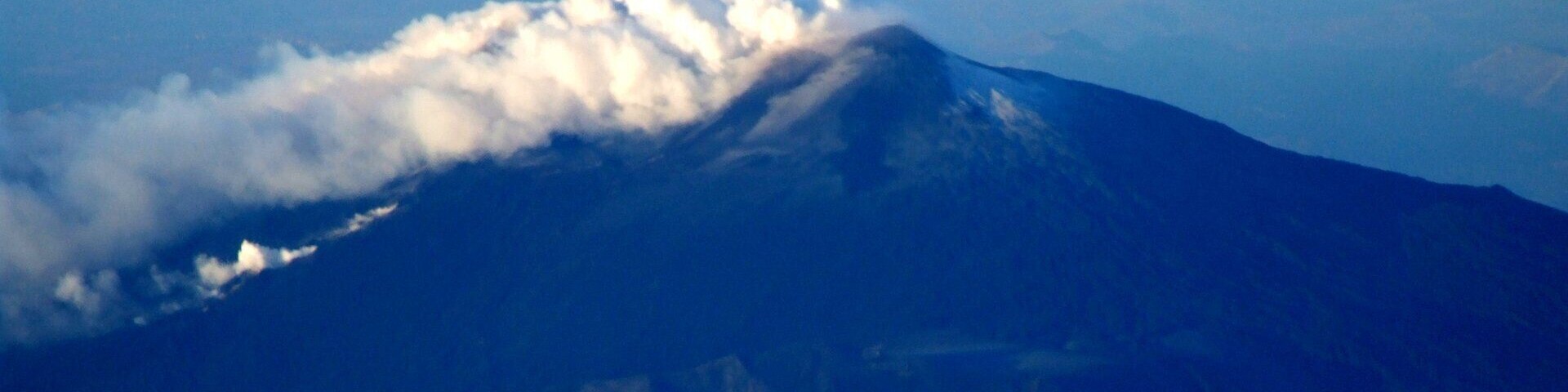 A mountain with a cloud-covered peak and a clear sky.