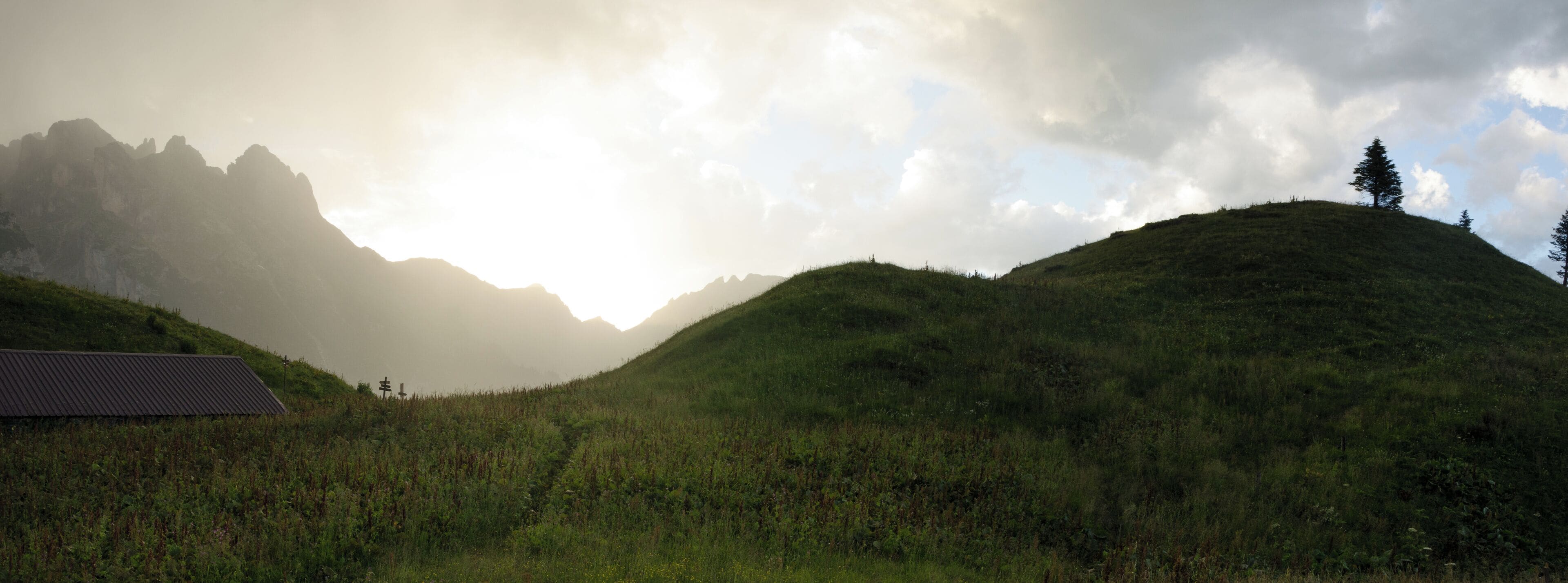 A mountainous landscape with a building on a hill and a tree on another hill.