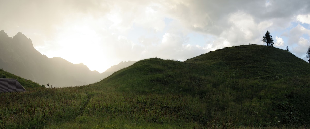 A mountainous landscape with a building on a hill and a tree on another hill.