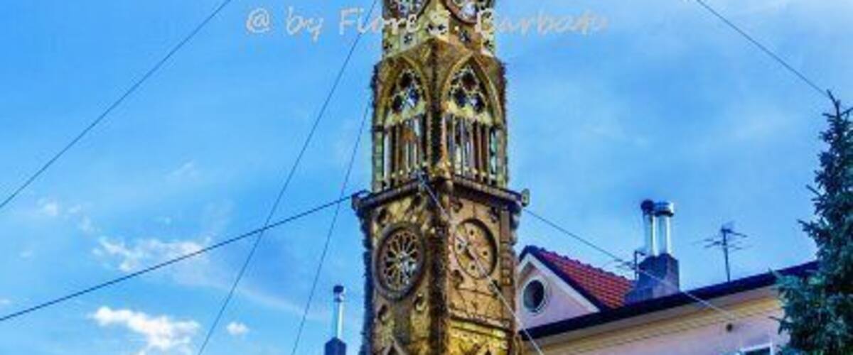 A tall, ornate clock tower with intricate designs and a pointed spire.