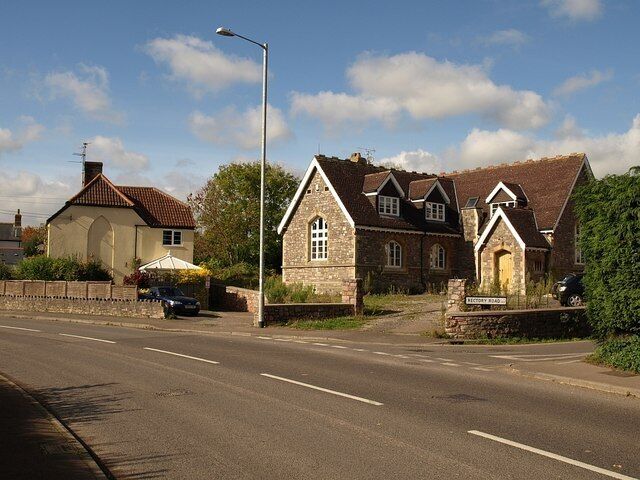 A rural road with stone houses, a clear sky, and a parked car.