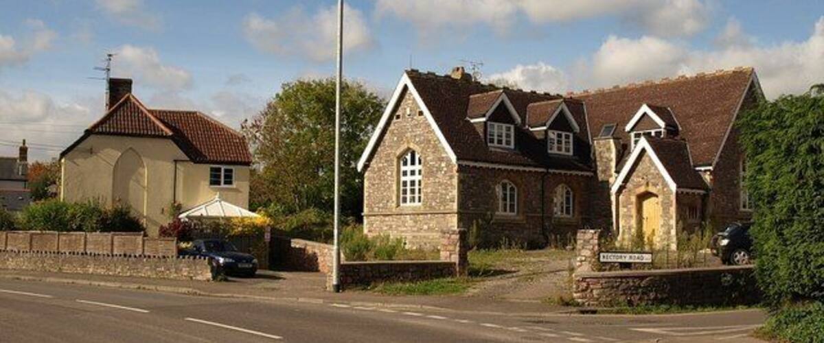 A rural road with stone houses, a clear sky, and a parked car.