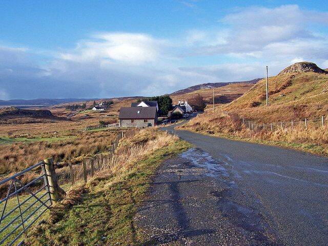 A rural road with houses and a hill in the background.