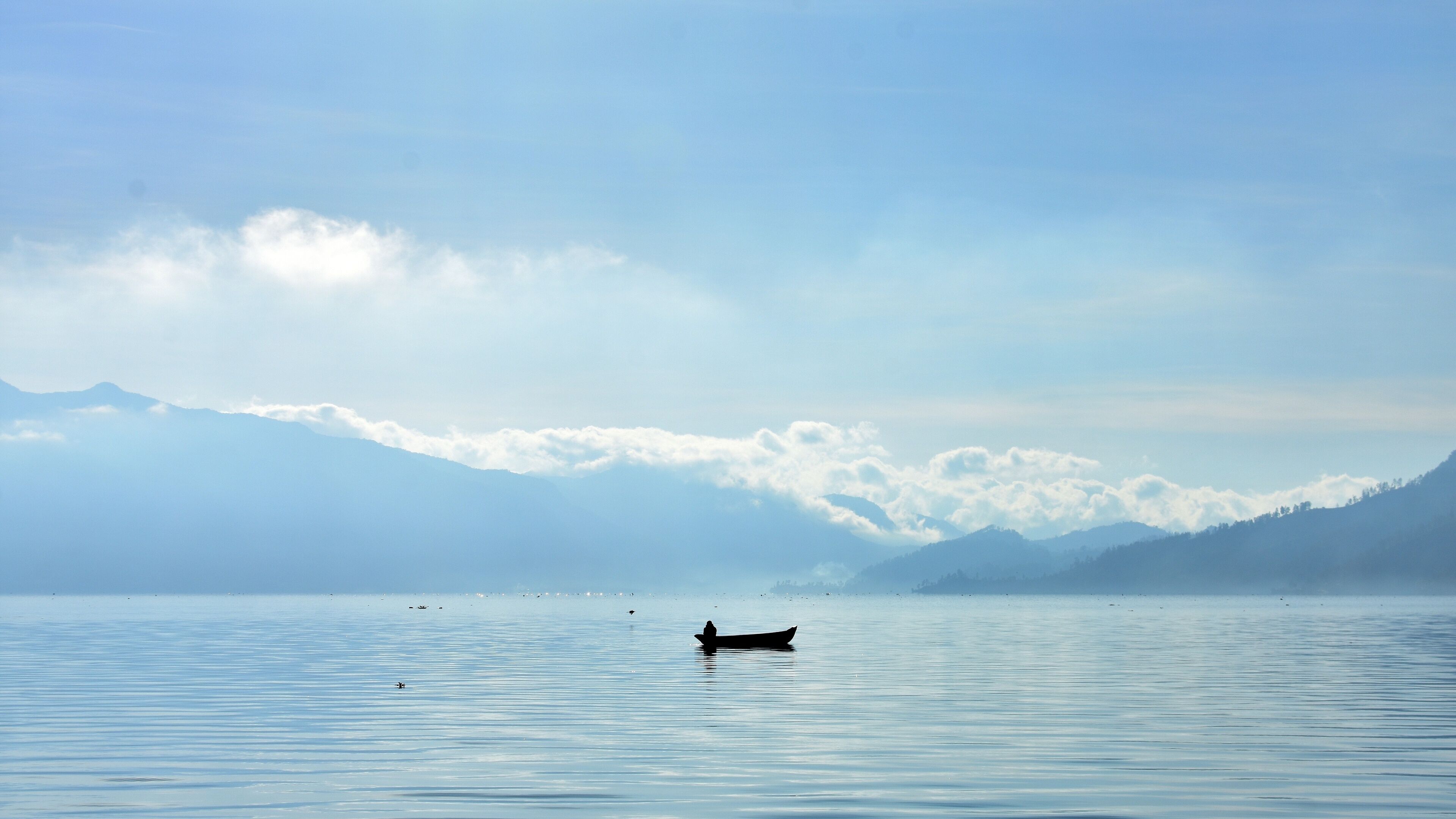 A calm lake with a boat and mountains in the background.