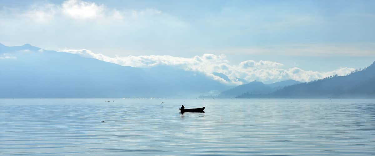 A calm lake with a boat and mountains in the background.
