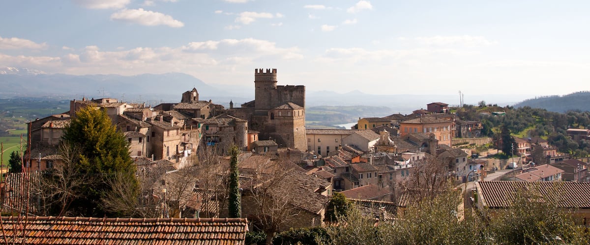 Un pueblo histórico con un castillo destacado, edificios con tejados de teja y un cielo azul despejado con nubes dispersas.