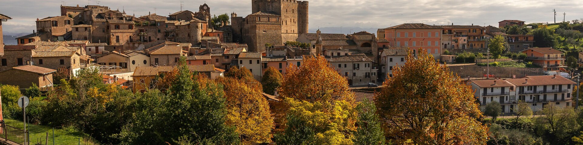 Un pueblo histórico con arquitectura medieval, que incluye un castillo destacado, rodeado de follaje otoñal.