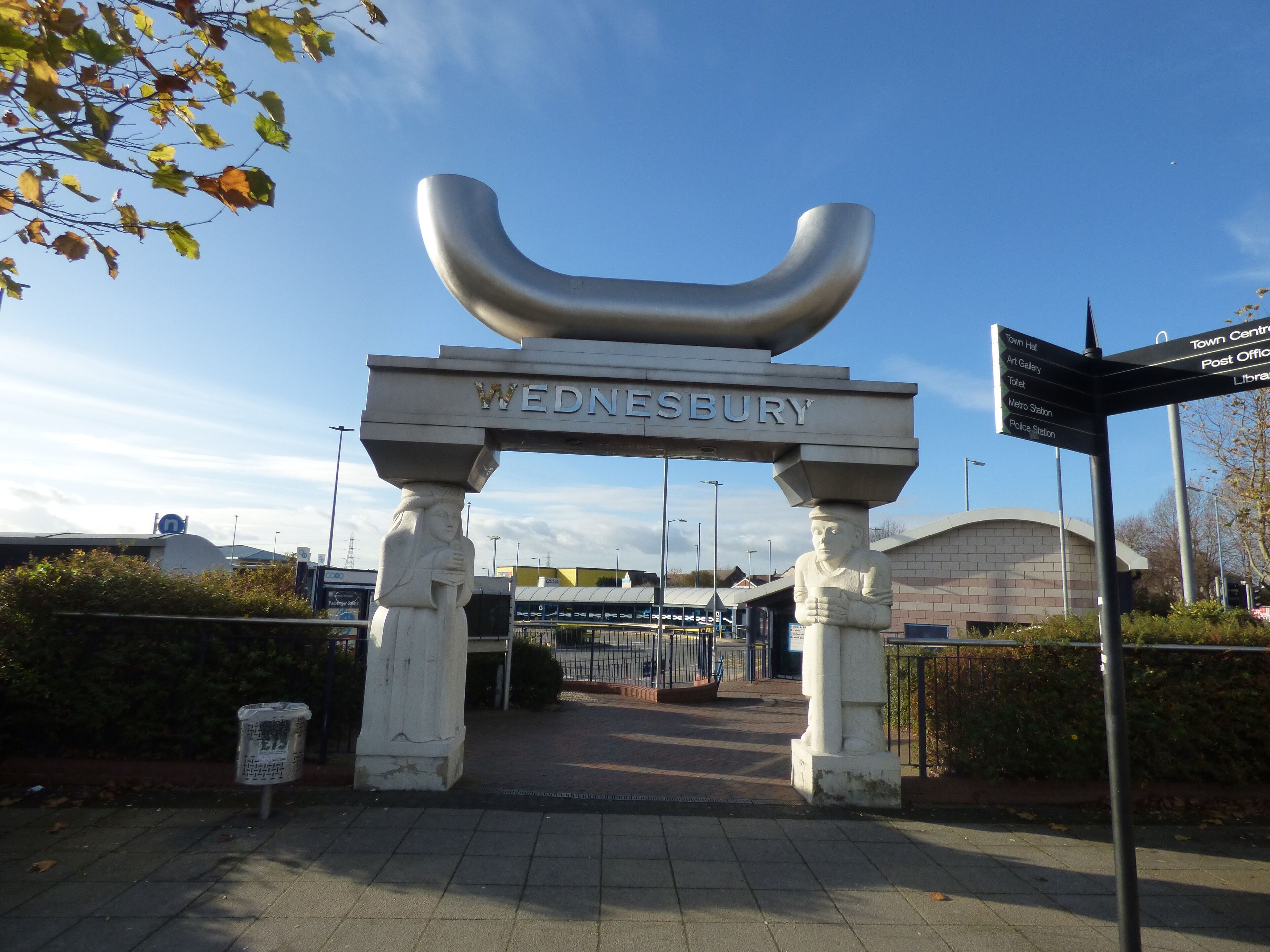 A look at Wednesbury Bus Station. It is close to the Morrisons supermarket. Located at Dudley Street and Holyhead Road. It's also quite close the outdoor market. Wednesbury Bus Station is a bus interchange in the town of Wednesbury, in the West Midlands region of England. It is managed by Network West Midlands. Local bus services operated by various bus companies serve the bus station which has 12 departure stands. The Midland Metro tram line stop at Wednesbury, Great Western Street is a short walk away. The rebuilt bus station opened in October 2004 as part of a major regeneration of the south side of Wednesbury town centre, which was completed three years later when a new Morrisons supermarket opened adjacent to the bus station. The Caryatid Gateway features two carved stone caryatids, one male and one female, each representing different aspects of Wednesbury history. The female figure represents Æthelflæd, daughter of King Alfred, who fortified Wednesbury against the Danes. The male figure represents a tube maker, Wednesbury being famous for the manufacture of tubes, the process having been patented in the nineteenth century by Cornelius Whitehouse. The tube reference is continued in the polished stainless steel inverted tubular arch 'carried' by the caryatids.