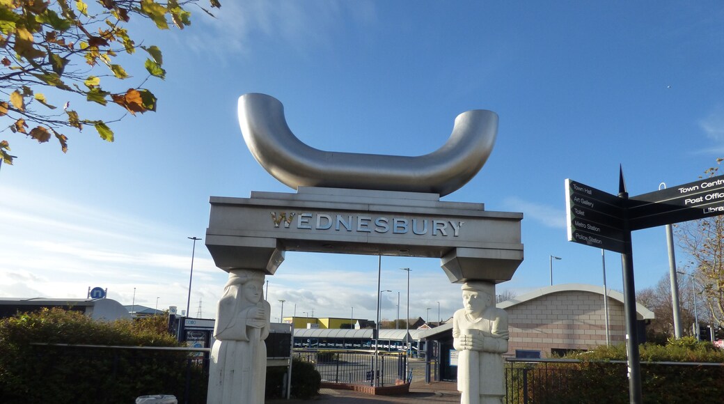 A look at Wednesbury Bus Station. It is close to the Morrisons supermarket. Located at Dudley Street and Holyhead Road. It's also quite close the outdoor market. Wednesbury Bus Station is a bus interchange in the town of Wednesbury, in the West Midlands region of England. It is managed by Network West Midlands. Local bus services operated by various bus companies serve the bus station which has 12 departure stands. The Midland Metro tram line stop at Wednesbury, Great Western Street is a short walk away. The rebuilt bus station opened in October 2004 as part of a major regeneration of the south side of Wednesbury town centre, which was completed three years later when a new Morrisons supermarket opened adjacent to the bus station. The Caryatid Gateway features two carved stone caryatids, one male and one female, each representing different aspects of Wednesbury history. The female figure represents Æthelflæd, daughter of King Alfred, who fortified Wednesbury against the Danes. The male figure represents a tube maker, Wednesbury being famous for the manufacture of tubes, the process having been patented in the nineteenth century by Cornelius Whitehouse. The tube reference is continued in the polished stainless steel inverted tubular arch 'carried' by the caryatids.