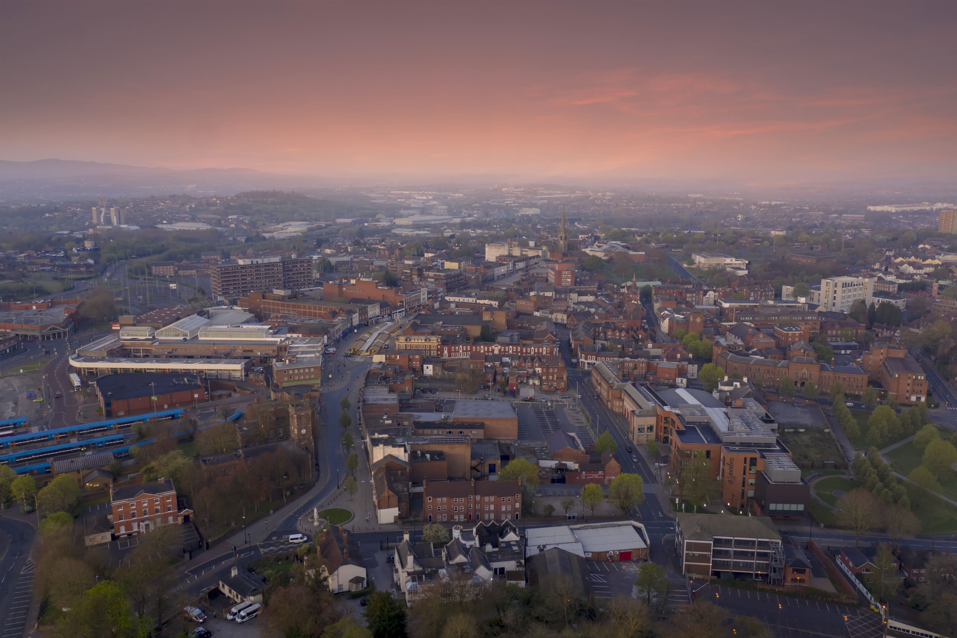 An aerial view of a city with a prominent church spire, a large industrial area, and a mix of residential and commercial buildings.