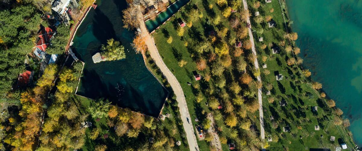 An aerial view of a park with a lake, pathways, and buildings.
