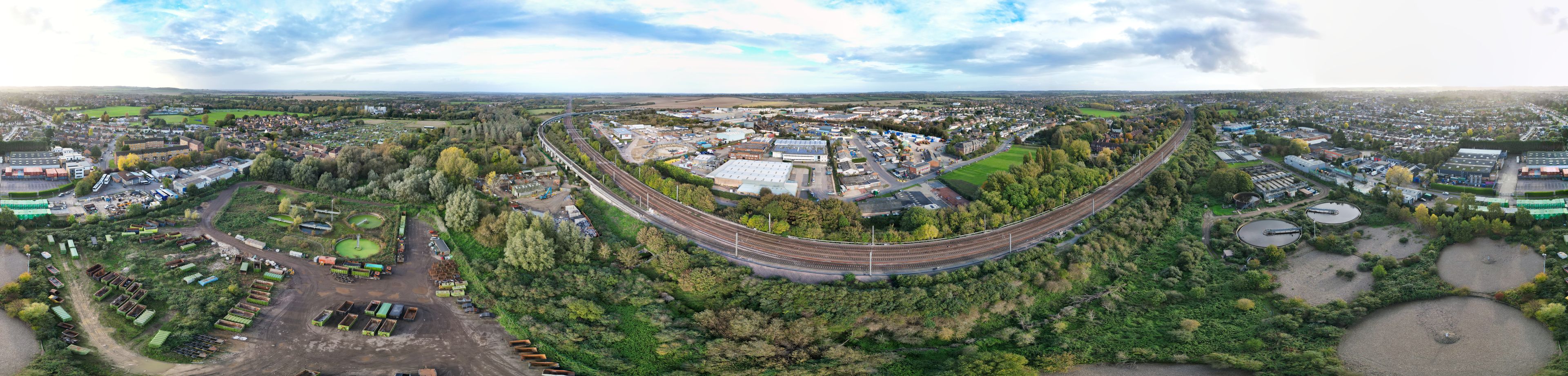 Trilhos de trem serpenteando por uma cidade cercada por vegetação e edifícios industriais.