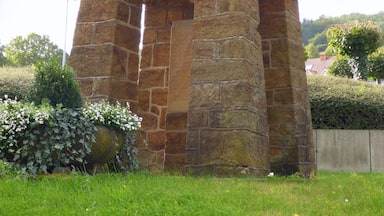 A stone monument with a statue of a man holding a child, surrounded by greenery.