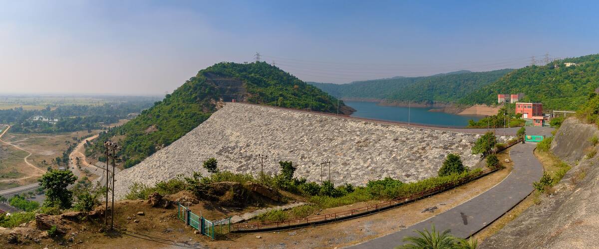 A large dam with a reservoir, a winding road, and a hilly landscape with sparse vegetation.