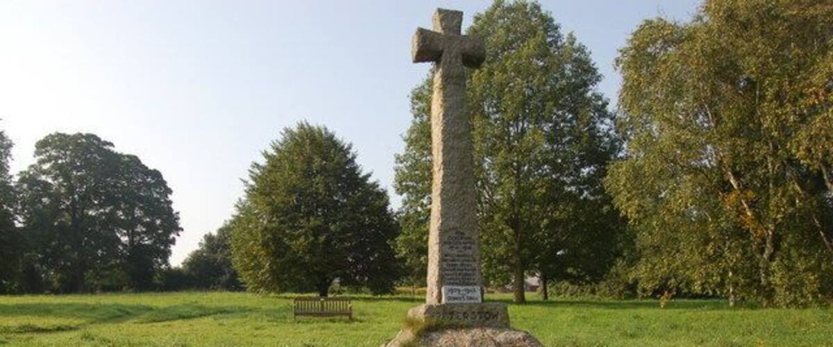 A stone cross monument in a grassy field with trees in the background.