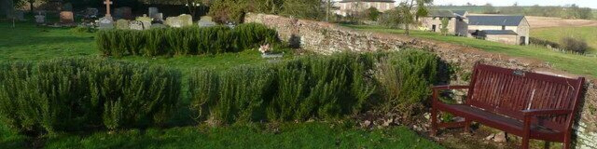 Un cementerio cubierto de césped con un banco de madera, setos cuidadosamente recortados y un muro de piedra.