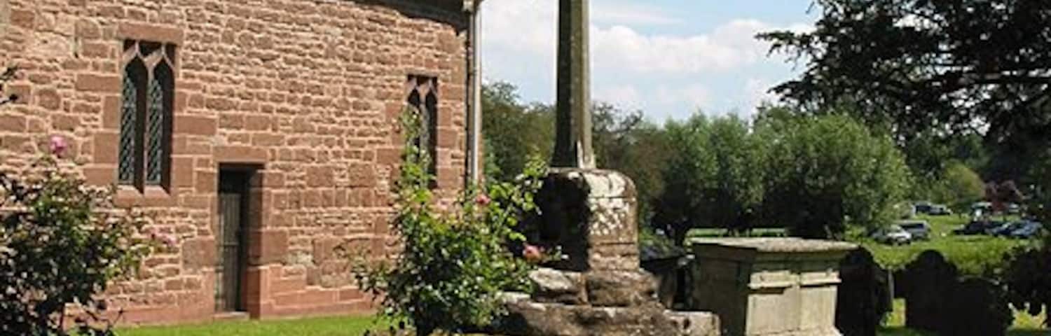 A church with a tall cross, stone walls, and a grassy lawn.