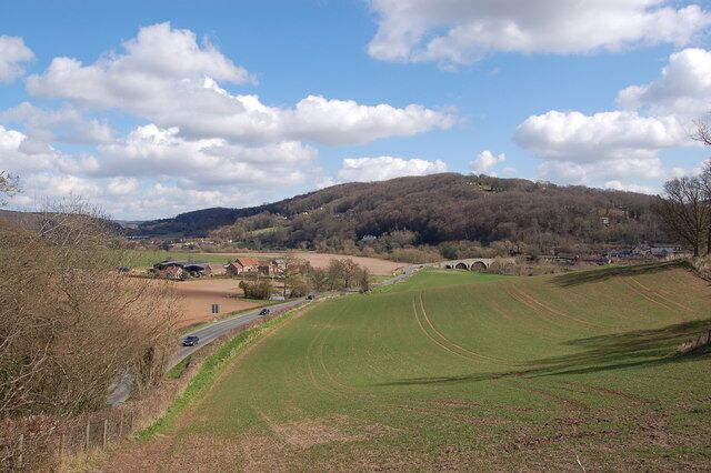 A rural landscape with rolling hills, a road, and scattered buildings.