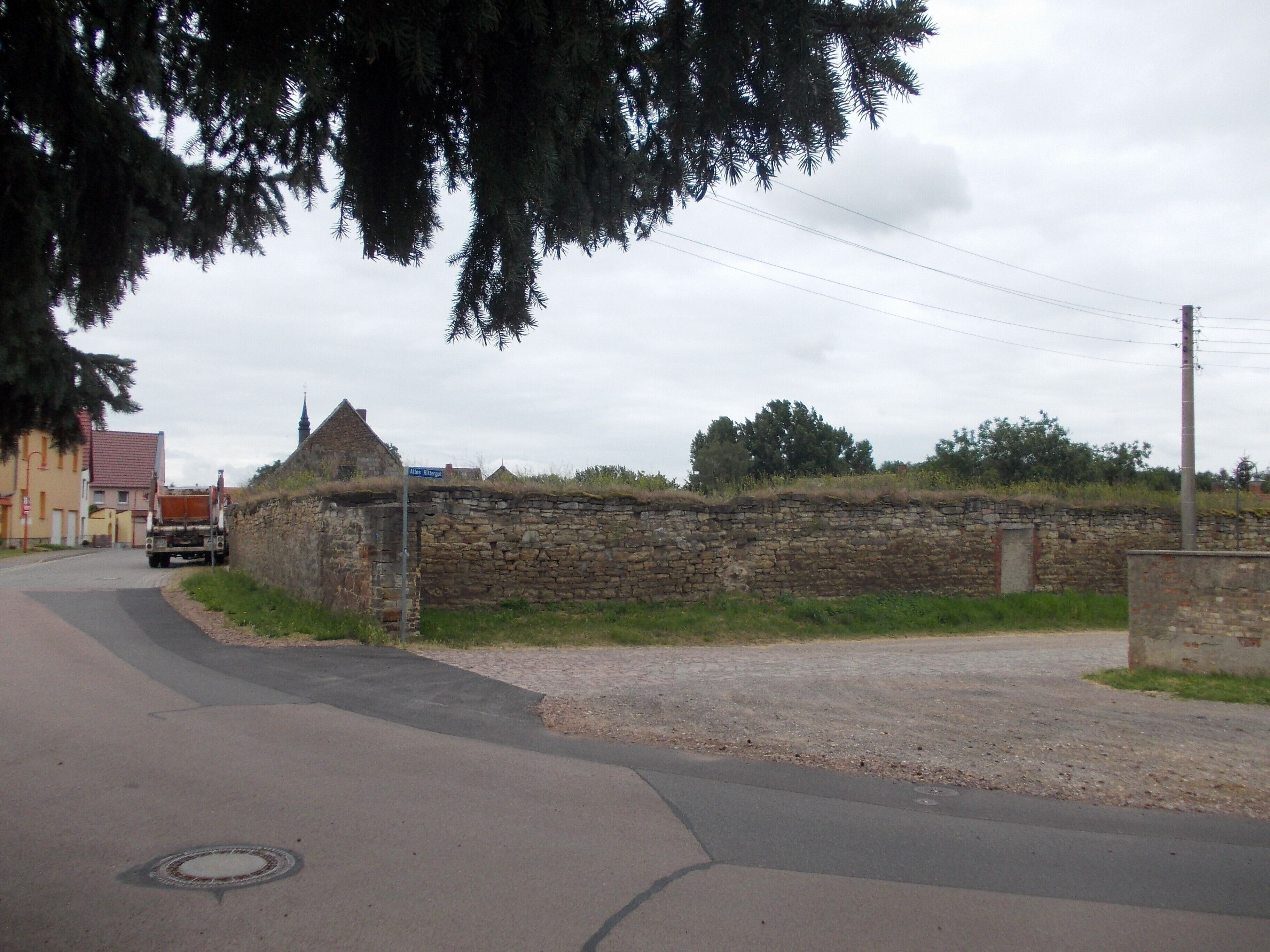 A rural road with a stone wall, a truck, and a church steeple in the background.