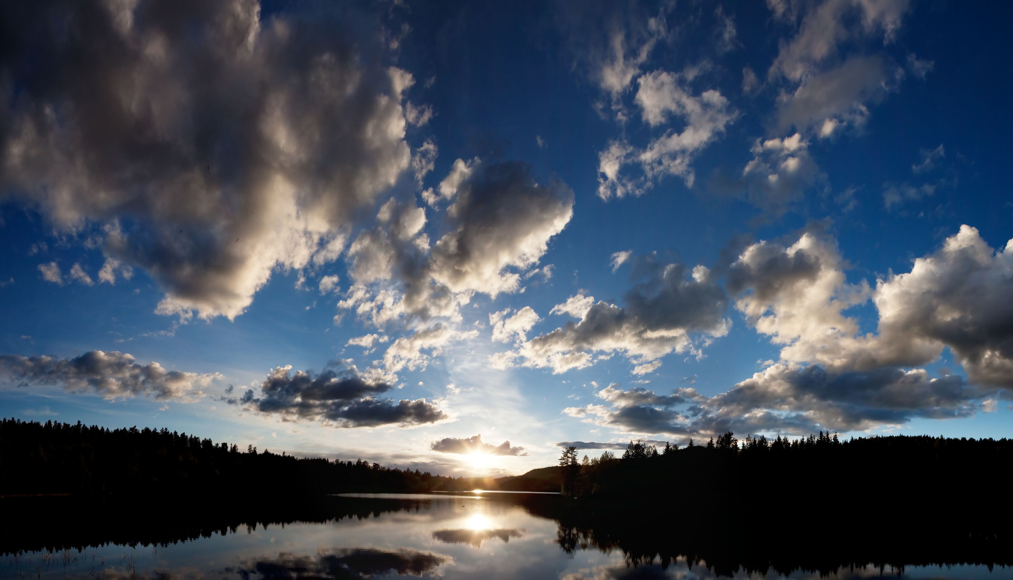 A lake with a forested shoreline and a sunset in the background.