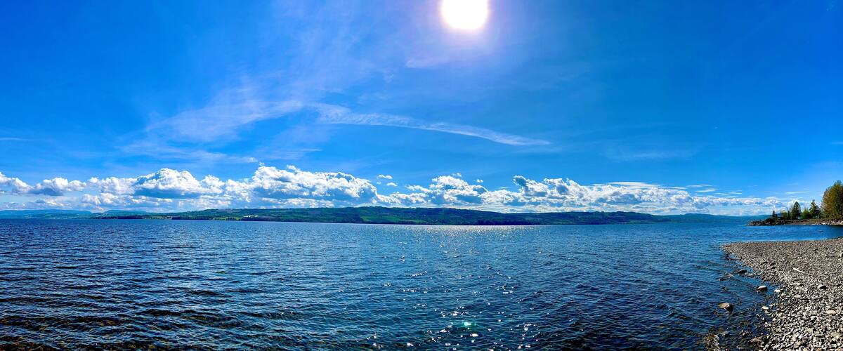 A lake with a rocky shoreline and distant mountains under a clear blue sky.