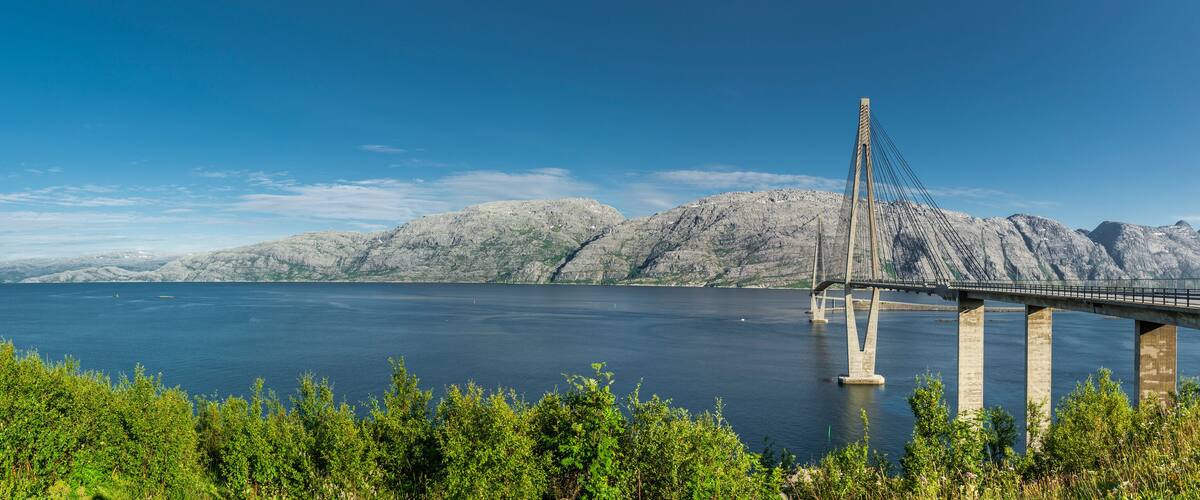 A cable-stayed bridge over a large body of water with mountainous terrain in the background.