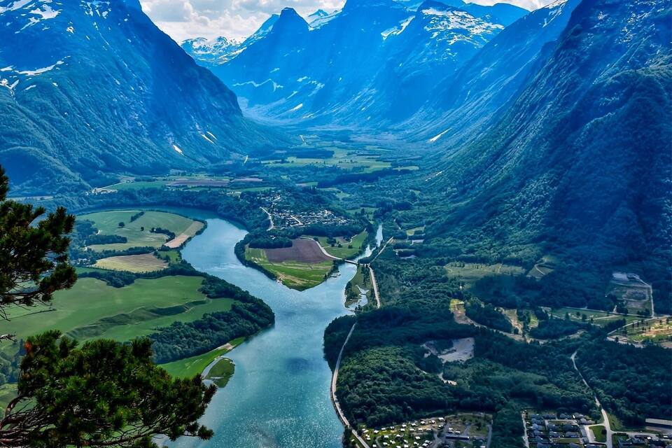 A mountainous landscape with a river winding through a valley, surrounded by forests and residential areas.