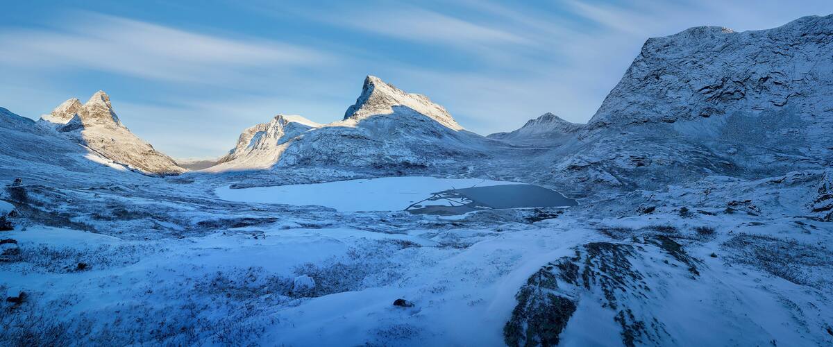 A snow-covered mountainous landscape with a frozen lake and rugged peaks.