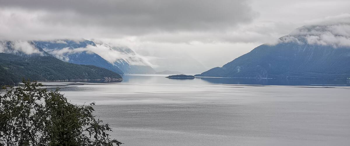 A calm lake surrounded by mountains with clouds above.