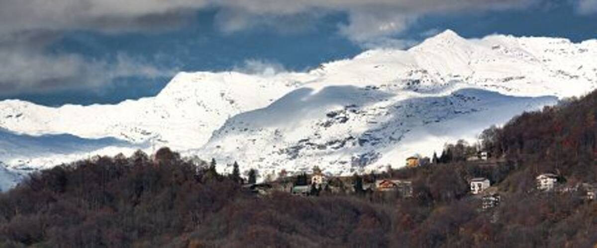 Snow-covered mountains, a cloudy sky, and a forested area with buildings.