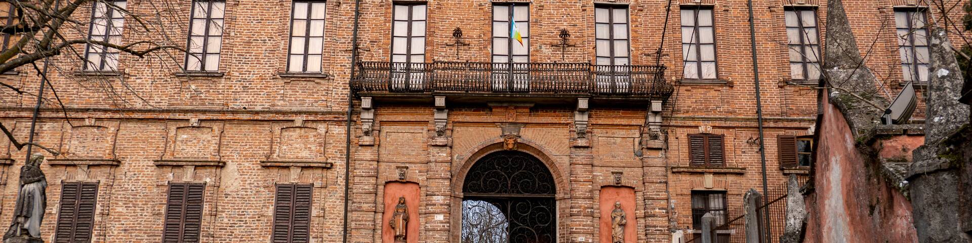 A historic brick building with a central archway, statues, and a flag.