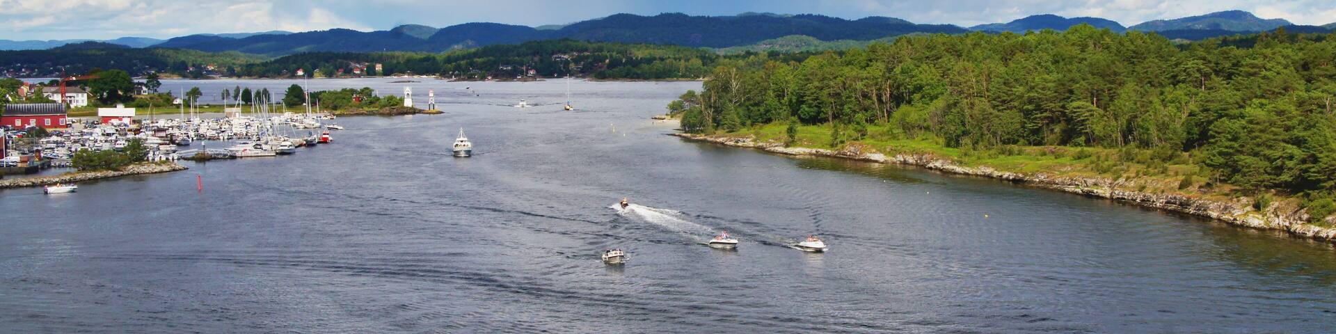 A river with boats, a marina, and a forested area with mountains in the background.