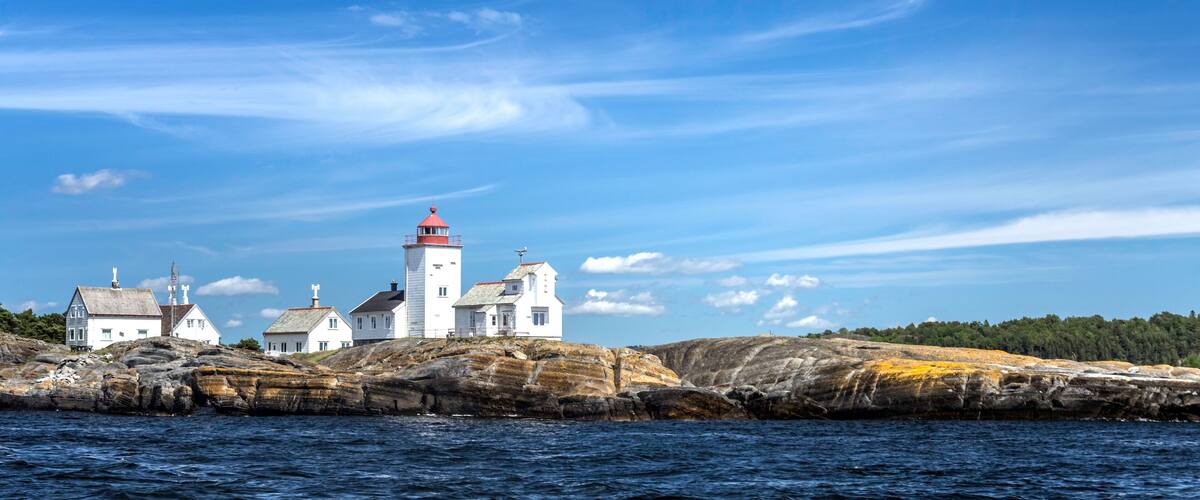 A coastal lighthouse with white buildings on a rocky outcrop.