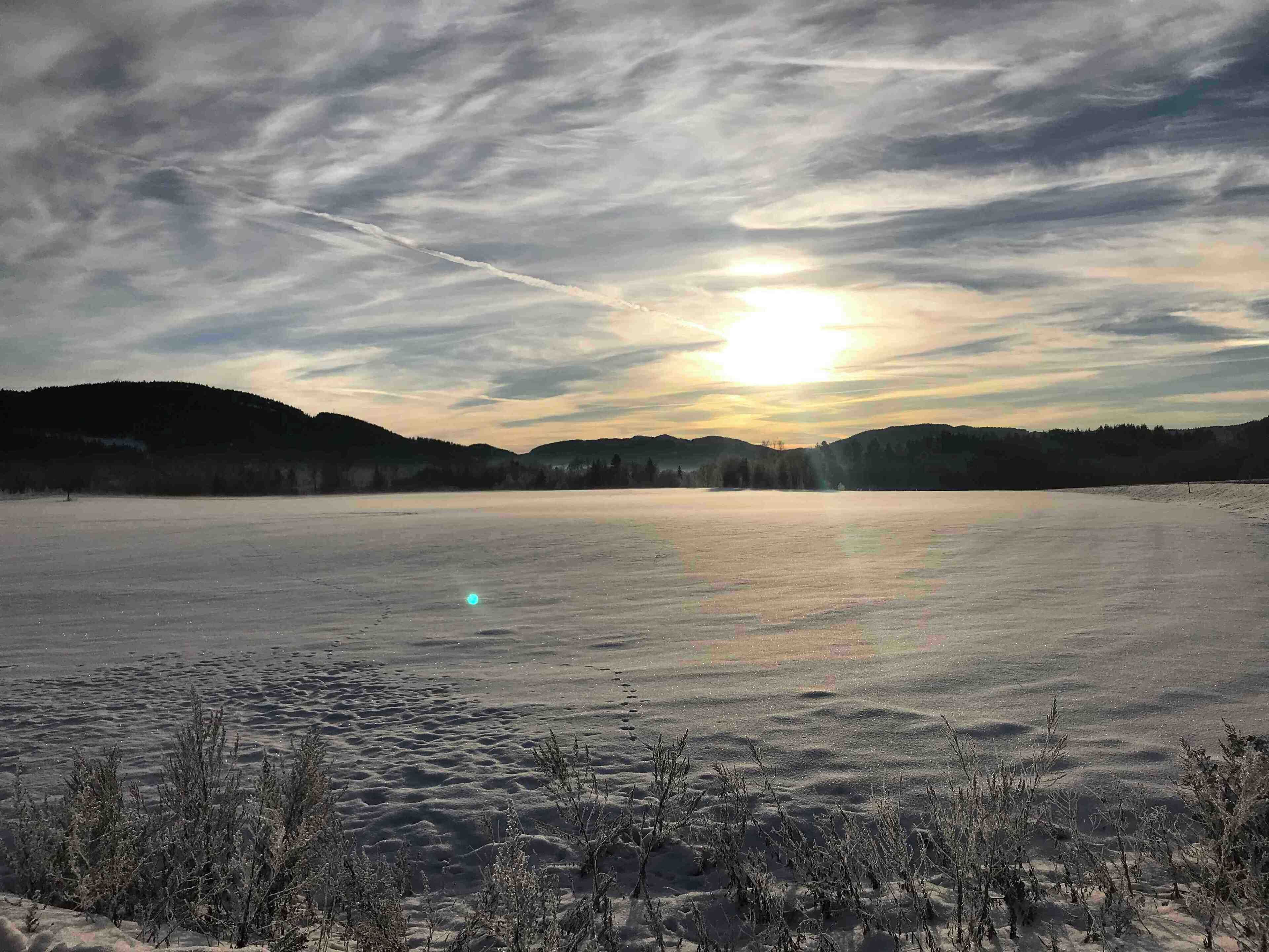 A frozen lake with a sunset, surrounded by hills and sparse vegetation.
