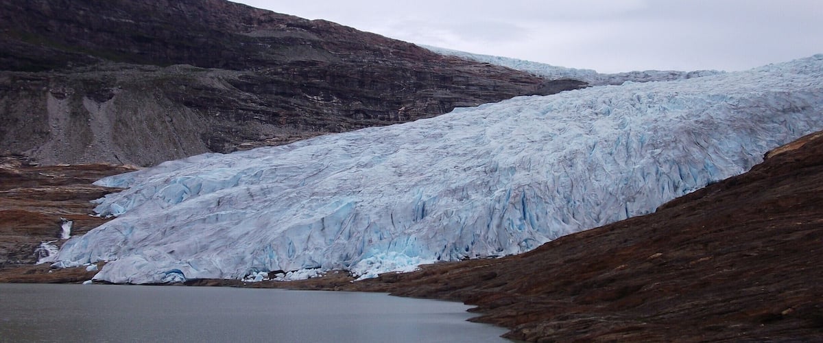 A glacier with a lake at its base, surrounded by rocky terrain.
