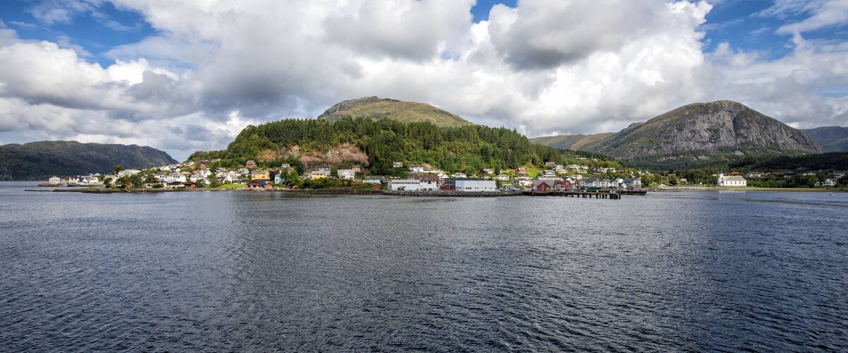 A calm lake with a small town on an island, surrounded by mountains and a partly cloudy sky.