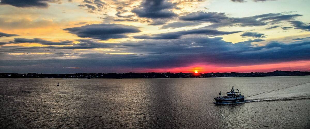 A sunset over a body of water with a boat and a sailboat.