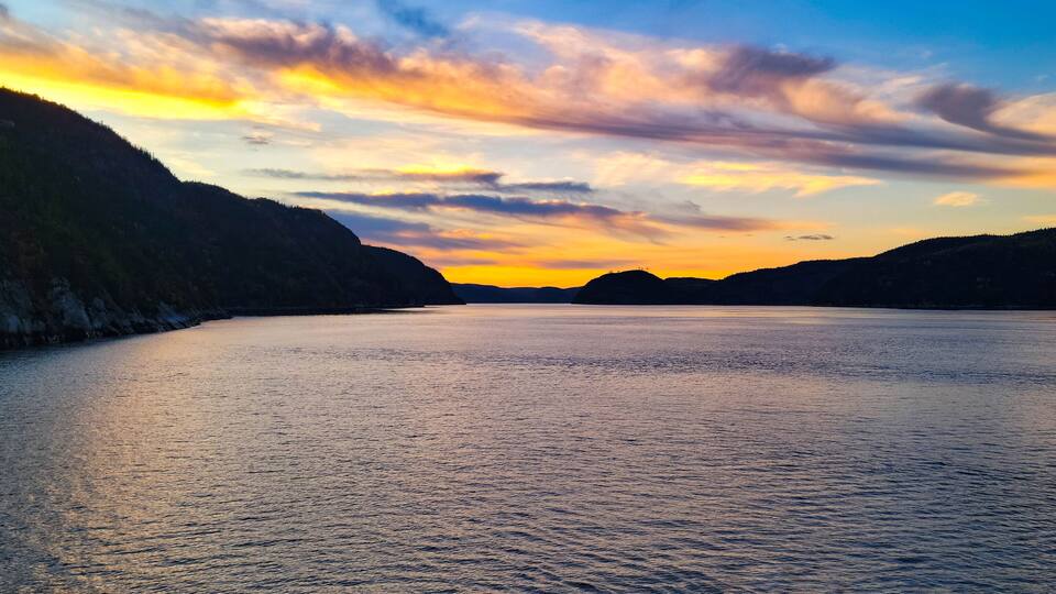A calm lake at sunset with hills on either side.