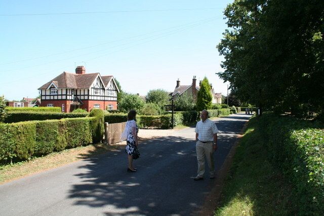 A rural road with a house on the left and a tree-lined path.